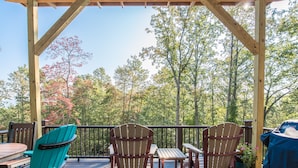 A wooden deck with a pergola, outdoor seating, and a view of trees. - Silver Lining Cabin -Natural light, Quiet, Hot Tub, Nature Trails, Pet door (Fletcher)