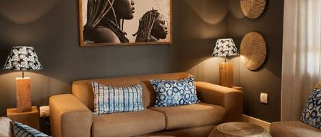 A modern living room with a brown sofa, patterned cushions, two floor lamps, a large framed artwork, and a textured wall decoration.