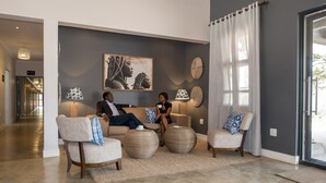 A modern living room with a sofa, two armchairs, and a coffee table. There is a painting on the wall, a lamp, and a large window with curtains. - Greenwood Manor Hotel Ndola (Ndola)
