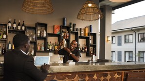 A bar area with a bartender and a customer. There are shelves with various bottles and a tablet on the counter. - Greenwood Manor Hotel Ndola (Ndola)