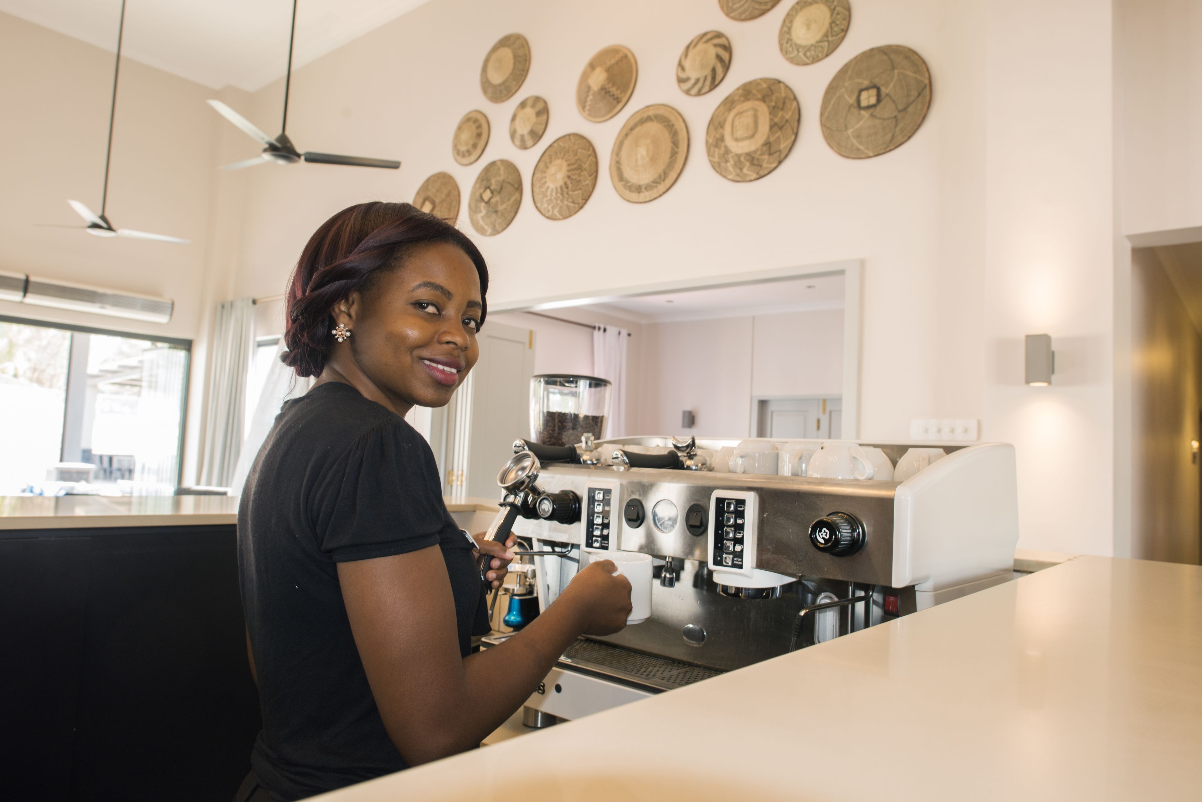 A person operating a coffee machine in a modern kitchen with decorative plates on the wall.