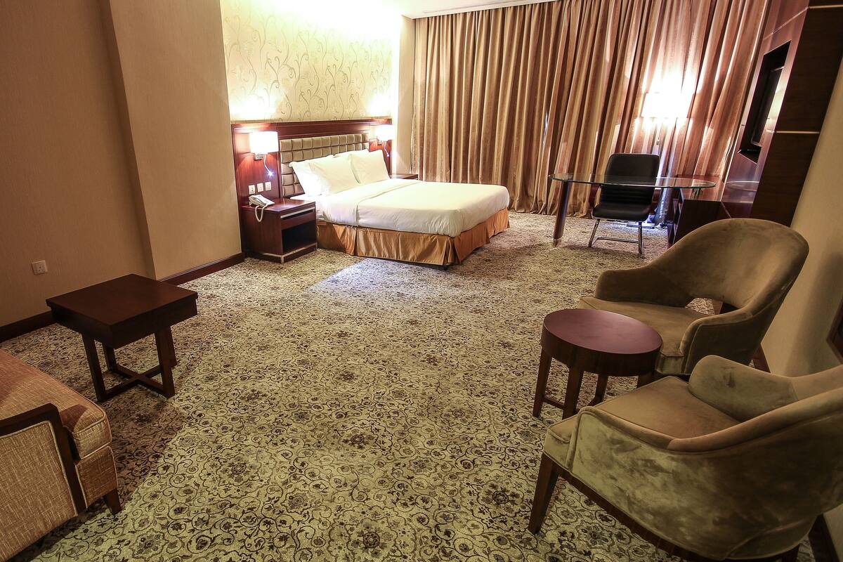 Et hotelværelse med en seng, et lille bord, to lænestole, en sofa og et tæppe på gulvet.