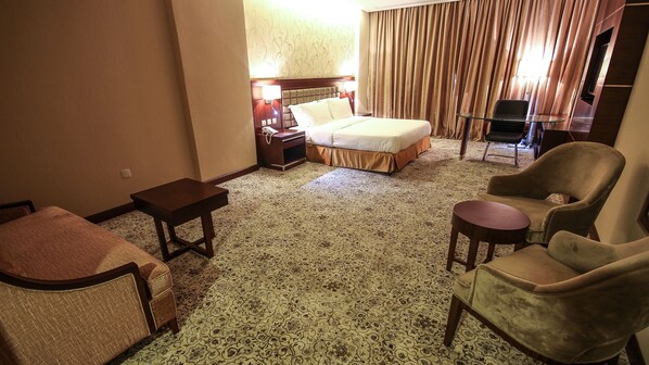 A hotel room with a bed, a small table, two armchairs, a sofa, and a carpeted floor.