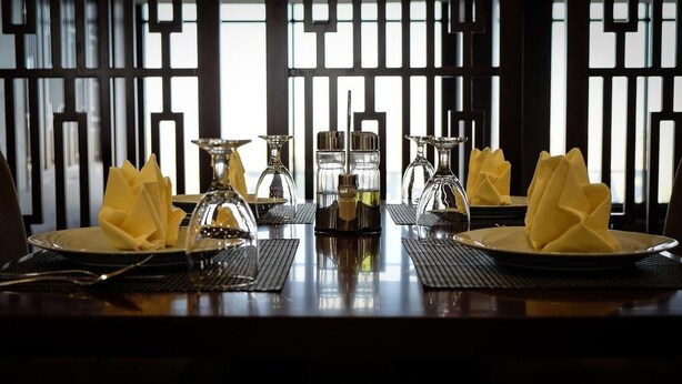 Mesa lista para comer, con platos, cubiertos y cristalería, y un fondo decorativo.