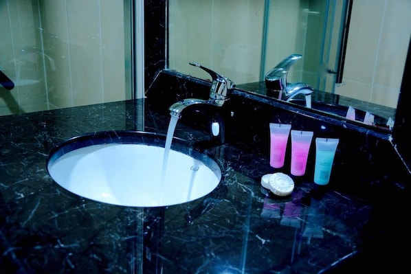 A bathroom sink with a marble countertop, a mirror, and three colorful bottles.