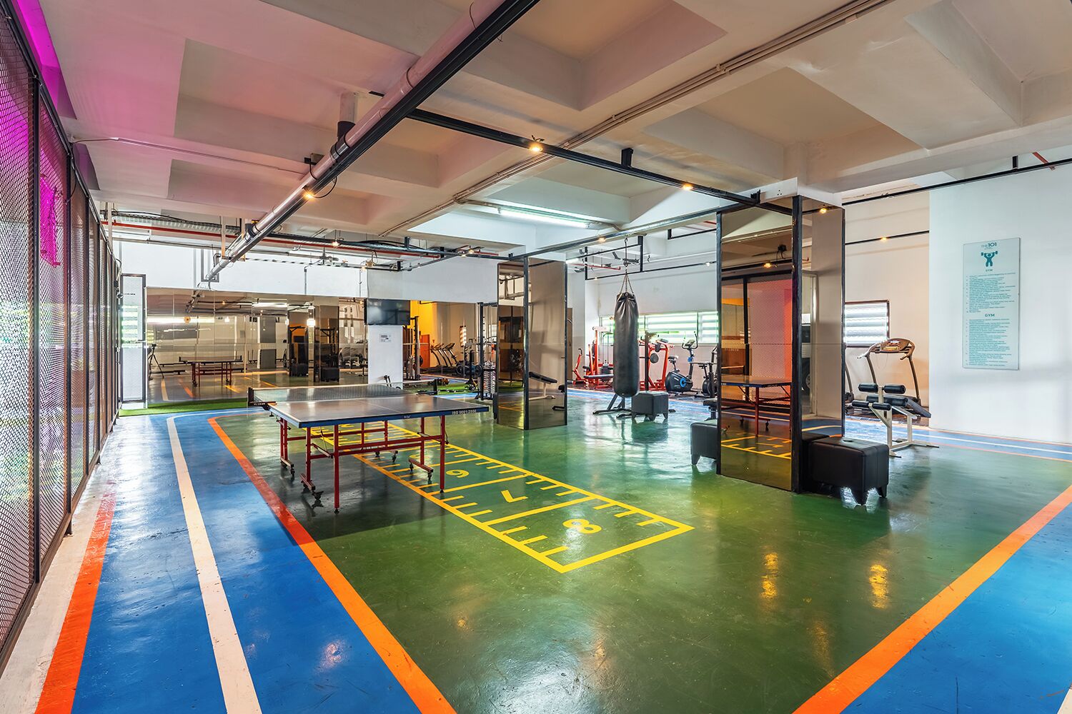 A spacious indoor area with a ping pong table, exercise equipment, and a green floor with yellow markings.