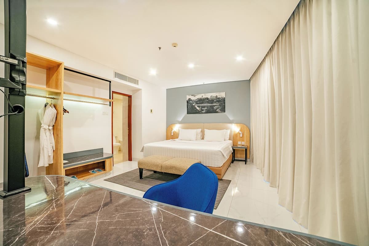 Quarto de hotel moderno com uma cama, área de estar, suporte para roupão e chuveiro.