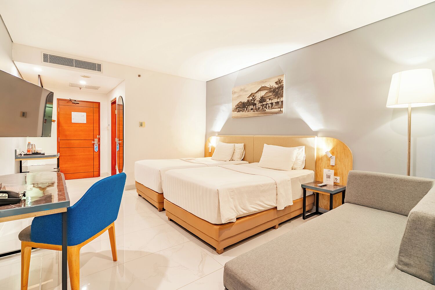A hotel room with a bed, a desk with a chair, a sofa, a lamp, and a picture on the wall.