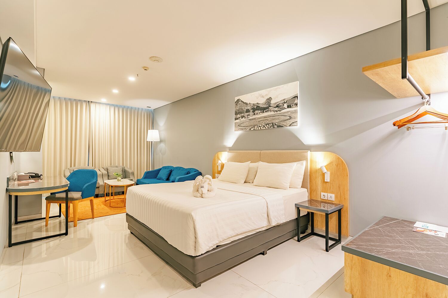 A modern hotel room with a bed, a desk, a chair, a sofa, and a bedside table.