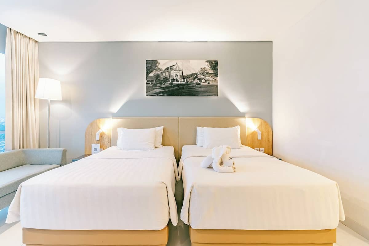 Quarto de hotel com duas camas, um sofá, uma luminária e um quadro na parede.