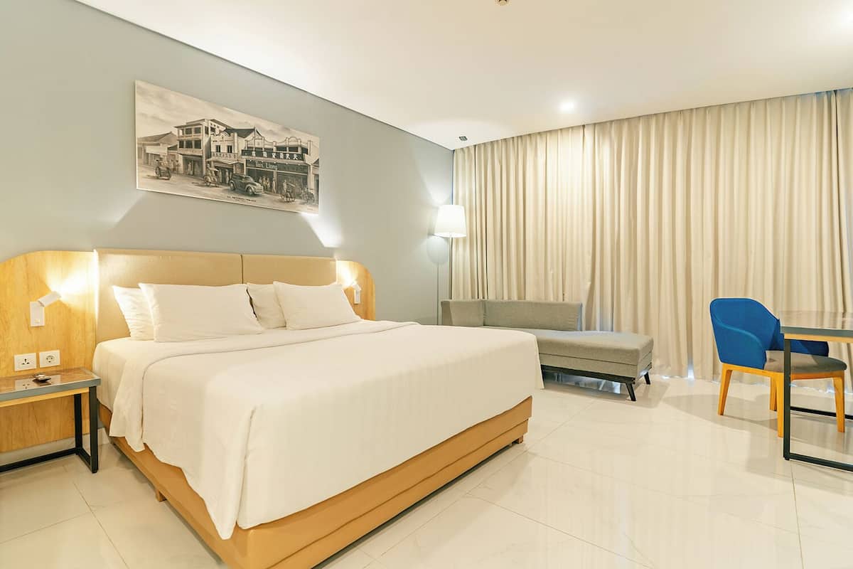 Quarto de hotel com cama, mesa de cabeceira, abajur, cadeira e um quadro na parede.