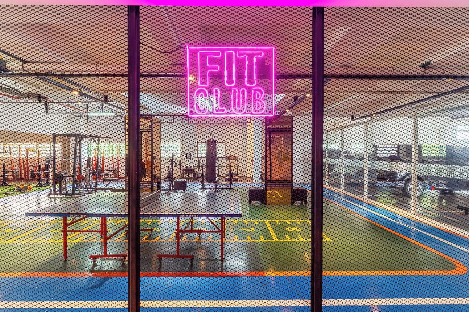 Un gimnasio con un letrero de neón que dice 'FIT CLUB' y varios equipos de ejercicio.