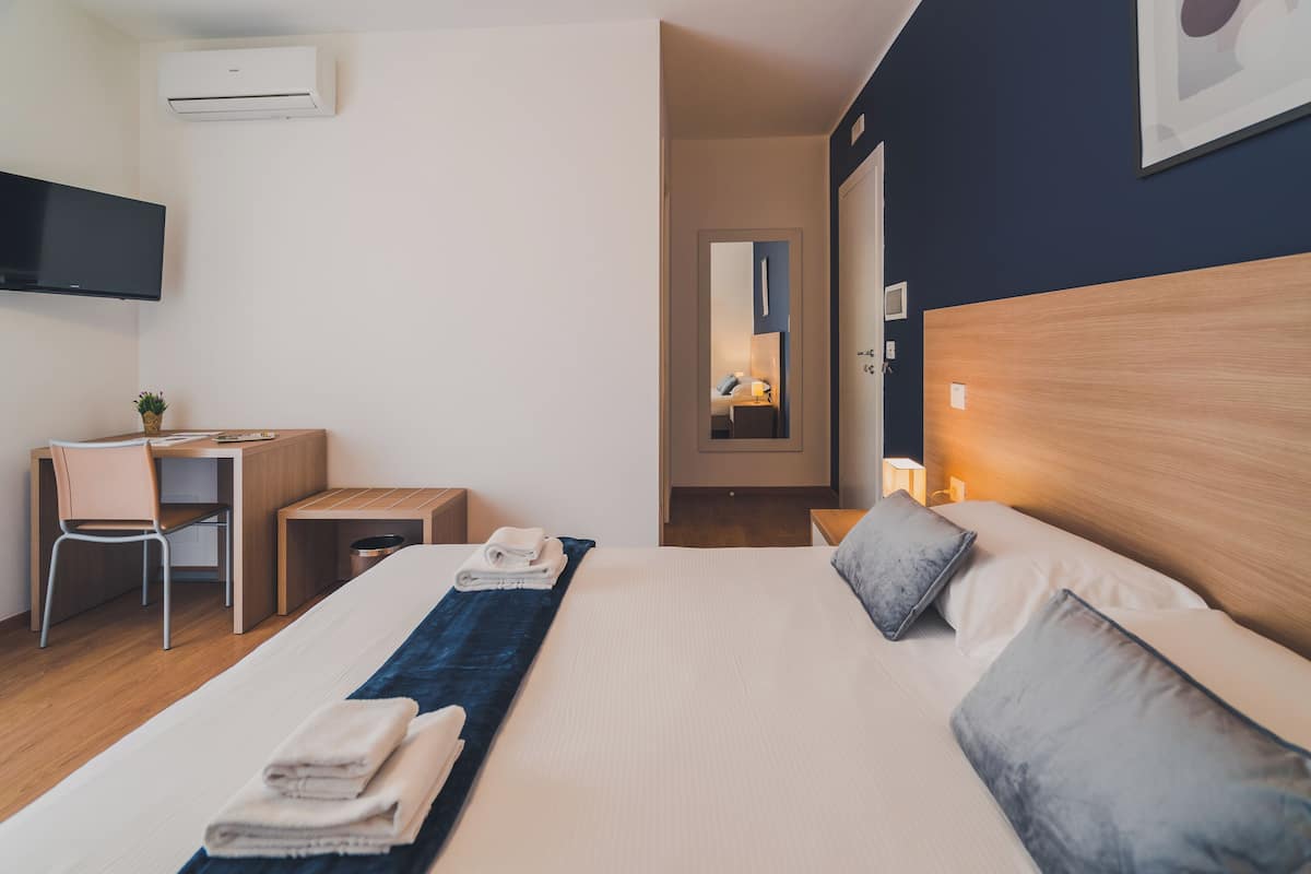 A hotel room with a bed, a desk, a chair, a TV, and a mirror.