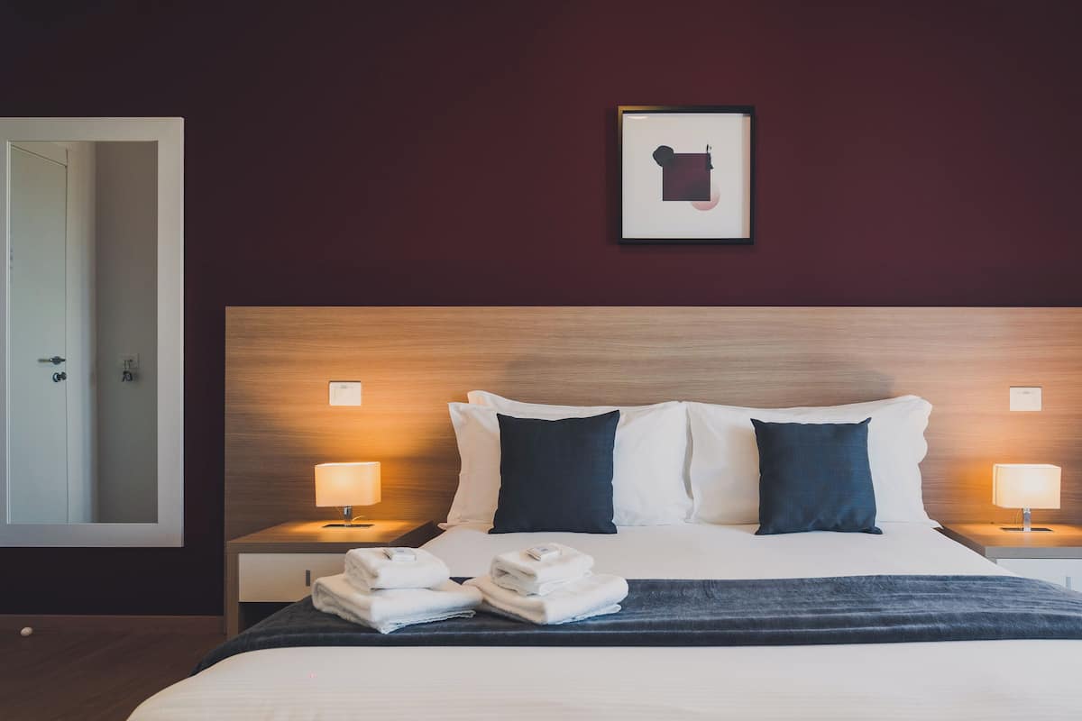A hotel room with a large bed, two bedside lamps, a framed picture on the wall, and a door to the left.