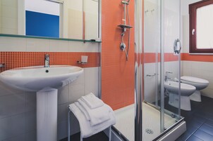 Un baño con ducha de vidrio, un lavabo blanco y dos inodoros.