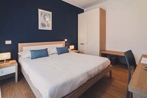 Quarto de hotel bem arrumado com uma cama grande, mesas de cabeceira, escrivaninha e uma cadeira.