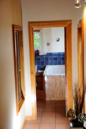 Un pasillo estrecho que conduce a un baño con una puerta de madera, una bañera blanca y una pared con azulejos azules.