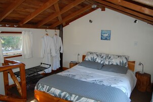 A bedroom with a wooden ceiling, a bed with floral bedding, a nightstand with a lamp, and a window with curtains.