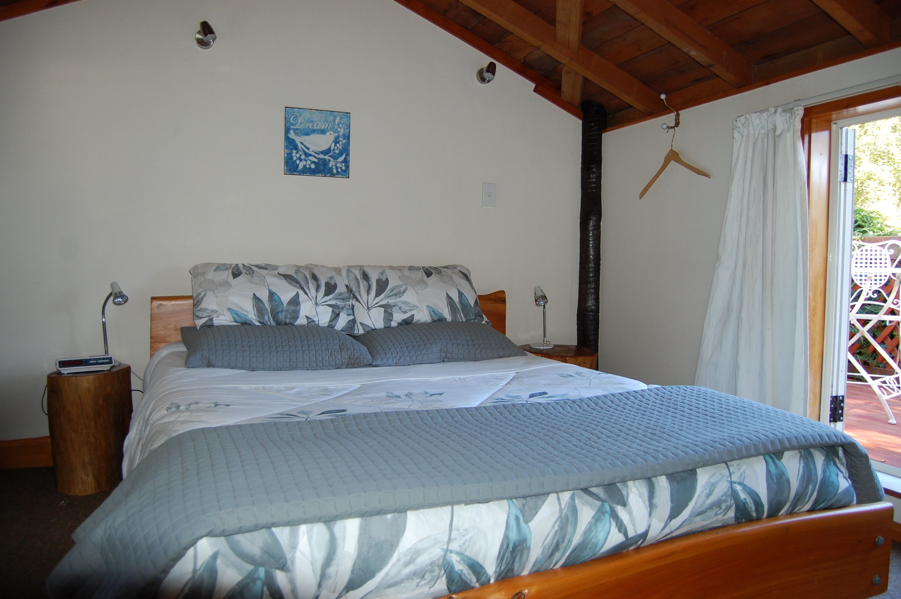 A bedroom with a bed, bedside tables, a hanging light, a wall clock, and a window with curtains.