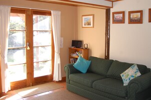 A cozy living room with a green sofa, a wooden bookshelf, and a door leading to a garden.