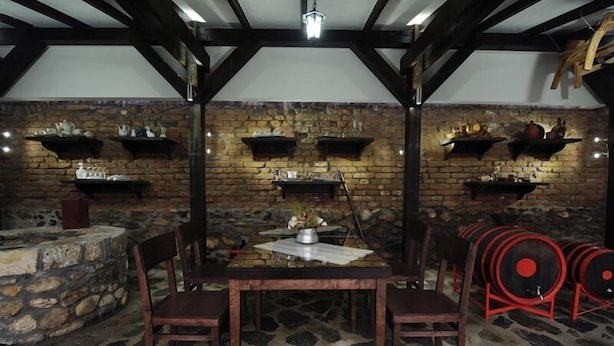 A rustic dining area with a stone wall, wooden beams, and a table with chairs. - Hotel Teatar (Bitola)