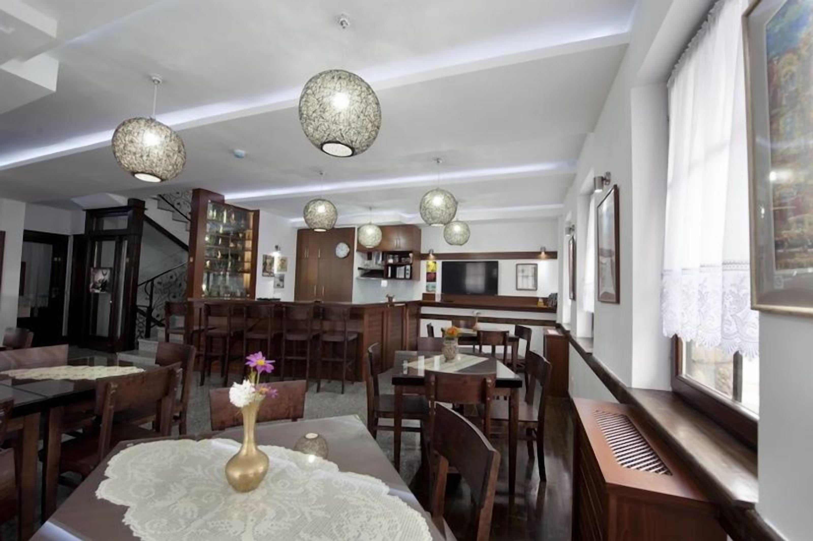 A spacious dining area with a high ceiling, pendant lighting, and a central table with a lace tablecloth.