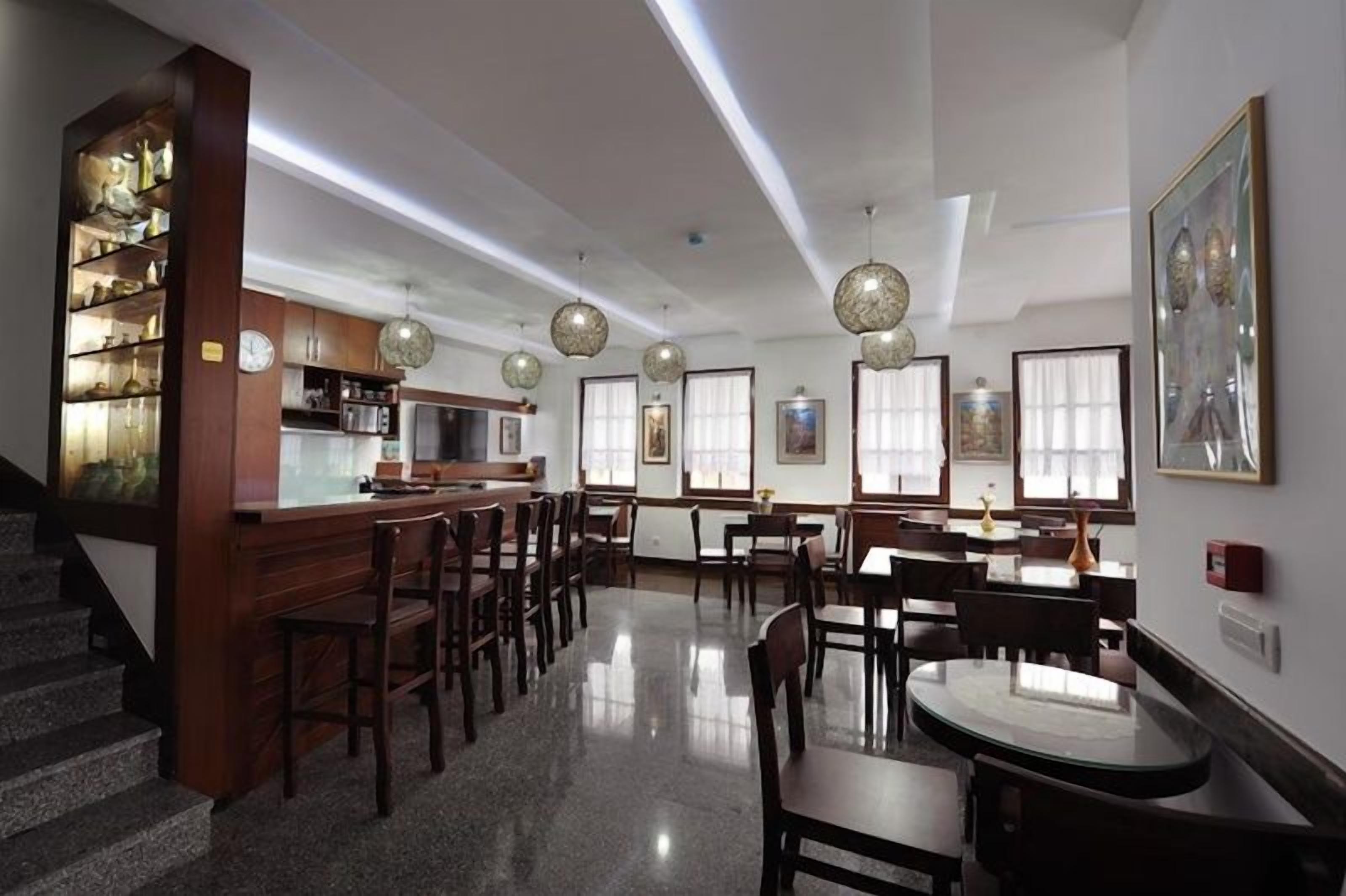 A spacious dining area with wooden tables and chairs, a kitchen area with cabinets and a refrigerator, and a staircase leading to an upper level.