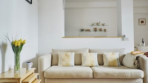 Een woonkamer met een beige bank, een houten salontafel en een vaas met gele bloemen.