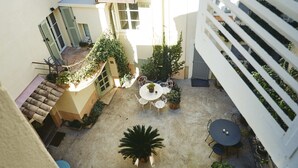 Een binnenplaats met een ronde tafel en stoelen, omringd door potplanten en een witte balustrade.