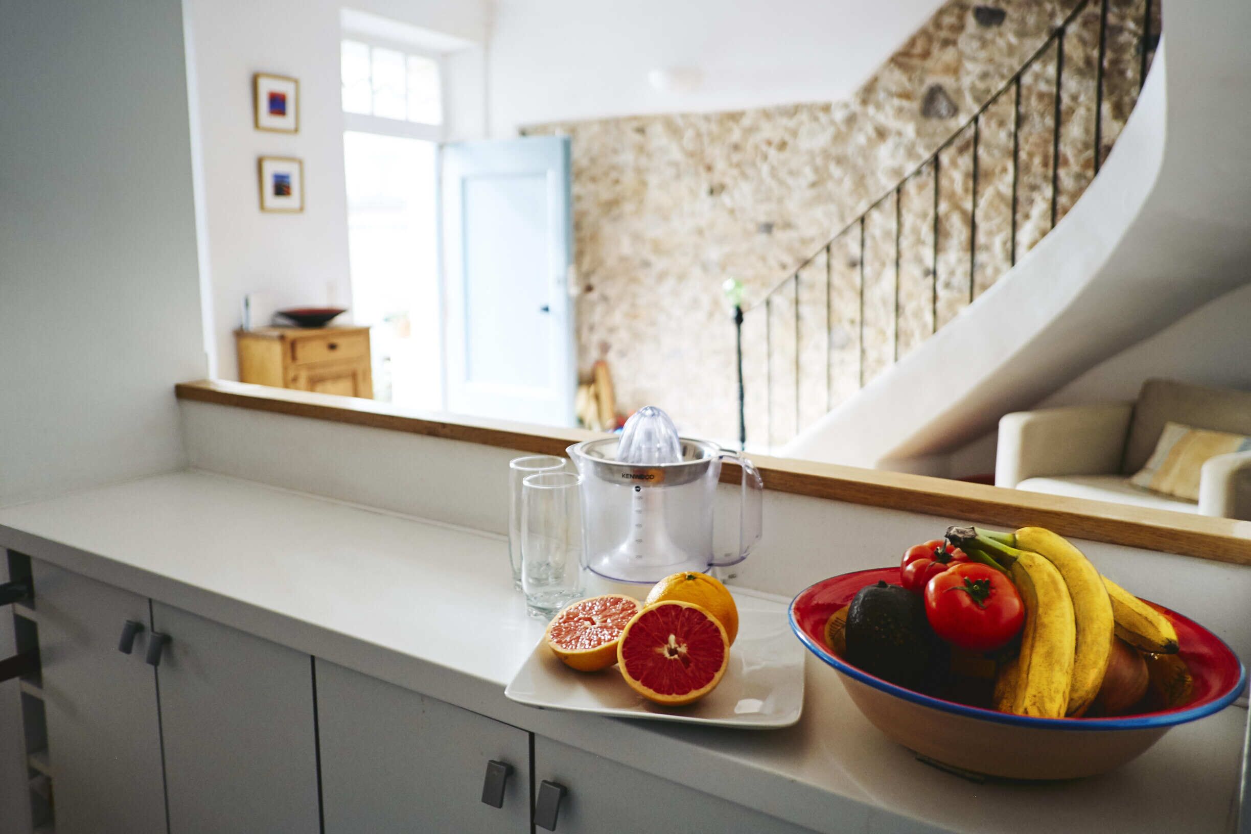 Un comptoir de cuisine avec un extracteur de jus, des verres et un saladier rempli de fruits.