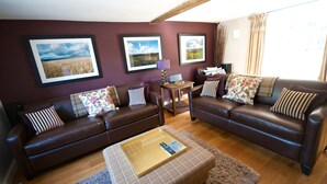 A living room with two brown leather sofas, a coffee table, and framed pictures on the wall. - Luxuriously Restored Family Friendly 300 year old English Country Cottage  (Westow)