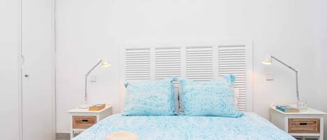 A bedroom with a bed, two bedside tables, a nightstand, a hat, and a lamp.