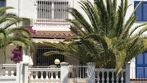Un edificio costero con fachada blanca, contraventanas azules y balcón con barandilla blanca.