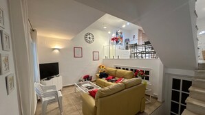 Una sala de estar con sofá, televisor y una escalera que sube a un nivel superior.