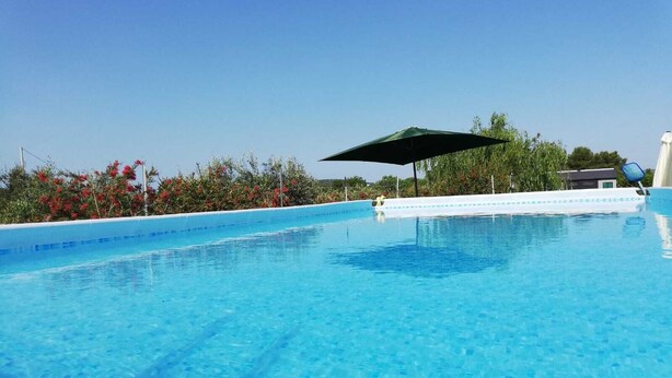 A clear blue pool with a shaded area and a white poolside structure. - Country house with swimming pool and barbecue in Alghero (alghero)