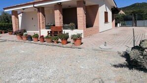 A single-story house with a tiled roof, a porch with potted plants, and a gravel driveway. - Country house with swimming pool and barbecue in Alghero (alghero)
