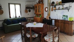 A living room with a dining table, chairs, a sofa, a cabinet, and a television mounted on the wall. - Country house with swimming pool and barbecue in Alghero (alghero)