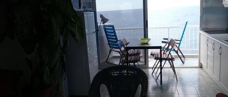 Un balcon avec vue sur la mer, une table à manger, des chaises, une plante en pot et un réfrigérateur.