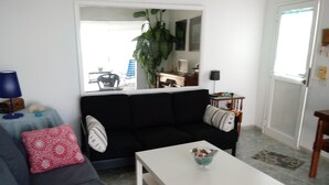 Una sala de estar con un sofá negro, una mesa de centro blanca y una mesita auxiliar azul con una lámpara.