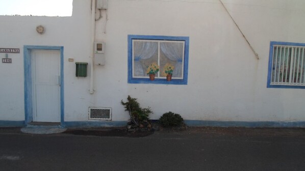 Un edificio con fachada blanca, puerta azul y una ventana con dos macetas.