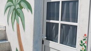Una puerta blanca con un ventanal, un árbol de palma pintado y una pequeña escalera que sube a la puerta.
