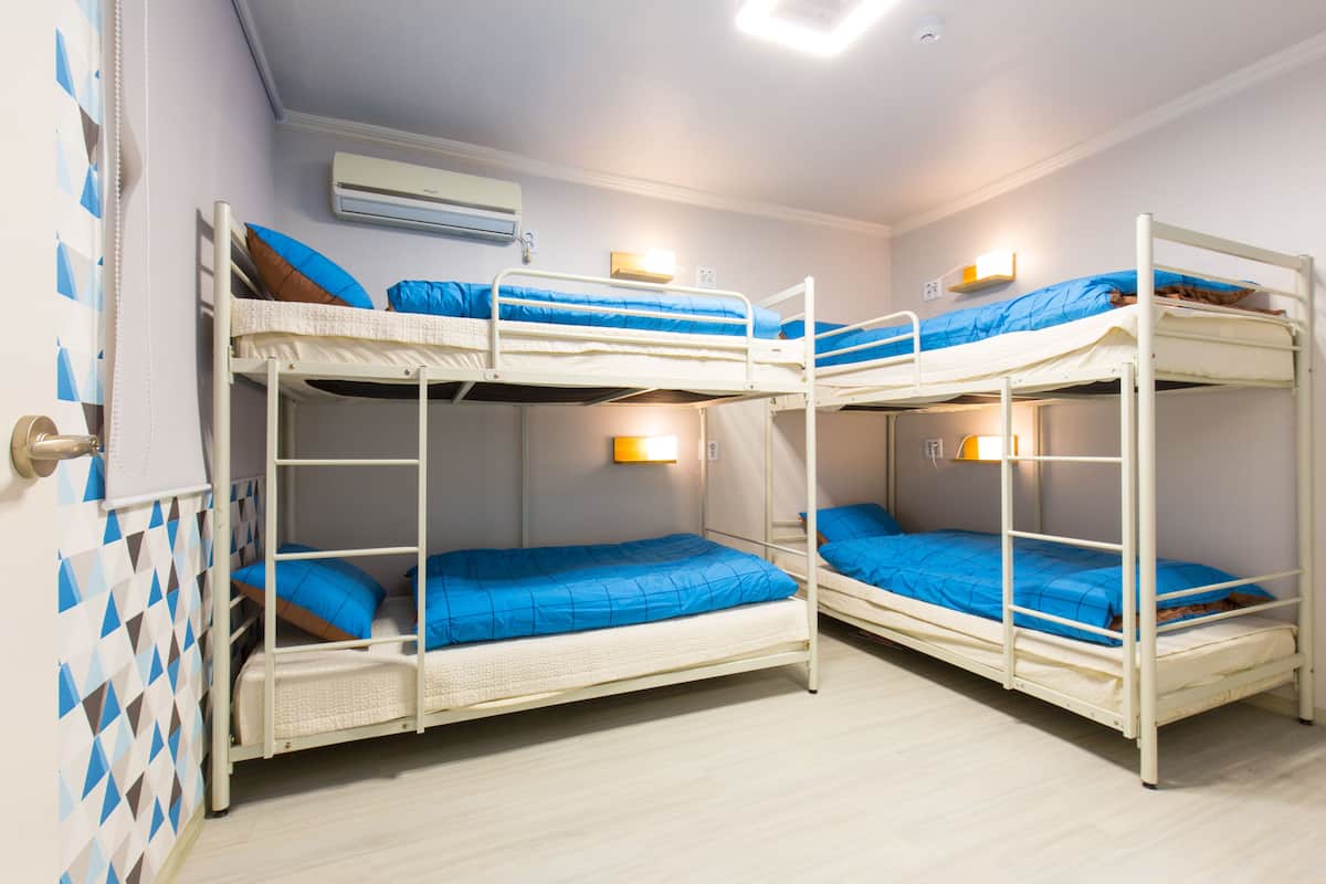 Une chambre avec trois lits superposés, chacun doté de draps bleus et d’une structure blanche. Un climatiseur mural est fixé au-dessus des lits.