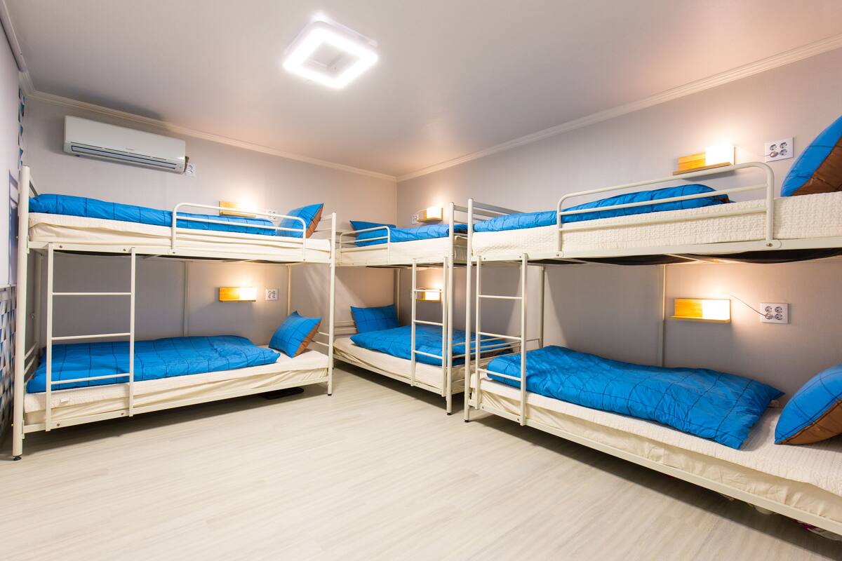 Une pièce avec quatre lits superposés, chacun doté de draps bleus et d’une structure blanche. Des lampes murales sont fixées au-dessus de chaque lit.