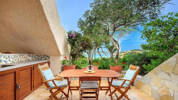 An outdoor dining area with a wooden table and chairs, surrounded by stone walls and potted plants.