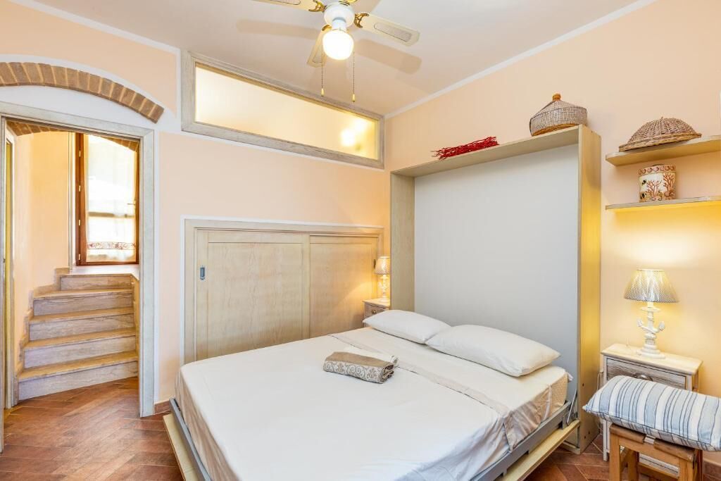 Quarto com cama, mesa de cabeceira, luminária, prateleira com objetos decorativos e escada para outro cômodo.