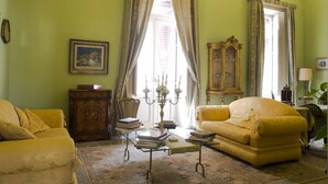 Una habitación con un sofá amarillo, un armario de madera, una mesa con libros y un espejo grande.
