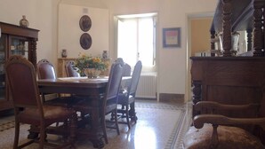 Un comedor con mesa de madera, sillas y una araña. Se ve una ventana con luz natural y un radiador en la pared.