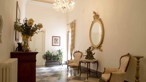 Un suelo a cuadros, un candelabro, un espejo grande y dos sillas en una habitación con un radiador y un jarrón de flores.