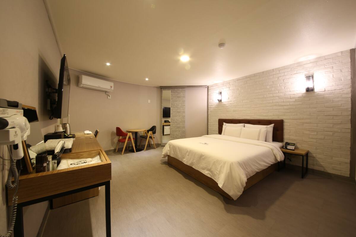Une chambre d’hôtel équipée d’un lit, d’un bureau avec un téléphone, d’une chaise et d’un téléviseur fixé au mur.