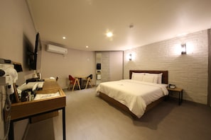Ein Hotelzimmer mit einem Bett, einem Schreibtisch mit Telefon, einem Sessel und einem an der Wand montierten Fernseher.